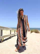 Vestido largo tejido con patrón geométrico en tonos marrón, beige, blanco y negro. Tiene escote en V y corte holgado.