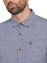 Camisa de manga larga celeste con botones marrones, bolsillo en el pecho y logo de pingüino bordado.