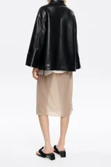 Chaqueta negra de cuero sintético con cuello camisero, cierre frontal con cremallera, bolsillos con cremallera en el pecho y mangas largas con cremalleras en los puños.