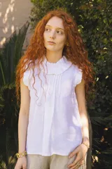 Blusa blanca sin mangas de lino natural con cuello fruncido y volados de encaje en las mangas.