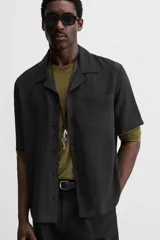 Camisa negra de corte relaxed fit, confeccionada en tejido con mezcla de modal. Tiene cuello bowling, manga corta, bolsillo de parche en el pecho y cierre frontal con botones.