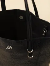 Bolso tipo tote negro de cuero vacuno con textura granulada, doble asa de hombro, apliques color marfil y logo JCH plateado en el frente. Incluye sobre desmontable en el interior.