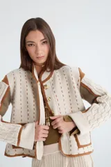 Chaqueta color beige con detalles en marrón, de lana con mangas tejidas con trenzas y cierre con botones.