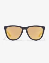 Lentes de sol Hawkers unisex, con montura cuadrada negra y cristales espejados color dorado.
