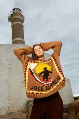 Sweater tejido de lana color marrón con cuello redondo y mangas largas. Presenta un diseño con un surfista y la inscripción "José Ignacio".