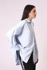 Camisa celeste de corte amplio, con cuello clásico, cierre frontal con botones y bolsillo en el pecho.