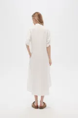 Vestido camisero midi negro de corte holgado, con cuello camisero, mangas cortas con trabillas, cierre frontal con botones, bolsillo en el pecho y bolsillos laterales.