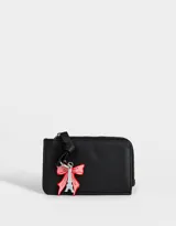 Monedero negro de cuerina con cierre circundante y charm colgante de moño rojo y torre Eiffel plateada.