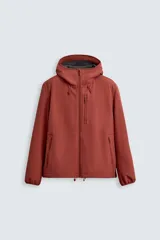 Cazadora color ladrillo de tejido técnico compacto con interior de forro polar. Tiene cuello con capucha ajustable, manga larga, bolsillos con cremallera en pecho y cadera, bajo ajustable con elástico y cierre frontal con cremallera.