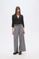 Pantalón gris de poliéster, de corte baggy, tiro alto, con pinzas frontales y bolsillos laterales.