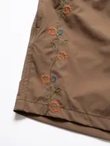 Short de baño marrón con bordado de enredadera en la pierna, cintura elástica con cordón regulable, bolsillos laterales y trasero con cierre.