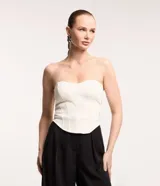 Blusa tipo corset color crema, sin breteles, confeccionada en crepé con bajo asimétrico alargado.