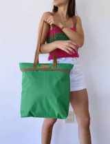 Bolso de lona color verde con manijas marrones y etiqueta con logo.