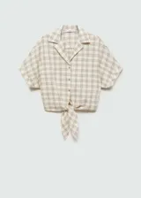 Blusa corta de manga corta con diseño a cuadros en tonos beige y blanco. Presenta cuello camisero, cierre frontal con botones y lazo en la parte inferior.