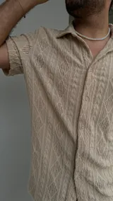 Camisa beige de crochet con cuello clásico y mangas cortas.