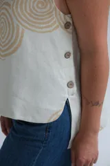 Musculosa color crudo de lino italiano con estampado de espirales color beige, escote redondo, corte irregular y botones de madera en los laterales.