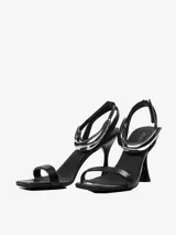 Sandalias de tacón negras con tira delgada sobre los dedos y pulsera tobillera con adorno tubular plateado.