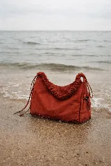 Bolso de nylon color terracota con textura sutil y manija fruncida. Tiene cordones ajustables a los lados y un bolsillo lateral con cierre.