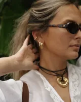 Collar con dije dorado irregular con agujero central, colgando de cordón negro ajustable.