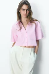 Camisa celeste de popelín con cuello solapa, escote pico y manga corta. Presenta dos bolsillos delanteros de parche y cierre frontal con botones.