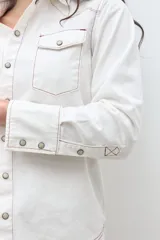 Camisa de jean color crudo, estilo western, con cuello y dos bolsillos frontales con tapa y botón. Presenta costuras contrastantes en tono rojizo.