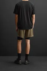 Shorts deportivos color verde oliva con calza interior negra, de tejido técnico ligero y elástico. Cuenta con cintura elástica ajustable con cordón, bolsillos laterales con cierre de cremallera, bajo con aberturas laterales y detalle de logo estampado.