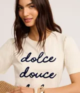 Remera color crema de algodón con cuello redondo y mangas cortas abullonadas. Estampa frontal con la frase "dolce douce dulce" en letras cursivas azul marino.