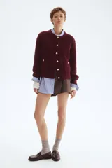 Cárdigan corto de punto acanalado en color vino tinto, con cuello redondo, cierre frontal de botones dorados y bolsillos de parche con botón en la parte delantera.