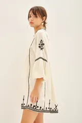 Vestido corto negro con bordado de hilo blanco a contratono, escote en V, manga larga y corte en la cintura.