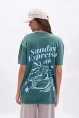 Remera verde con corte oversize y estampa en la espalda con la frase "Sunday Expresso Club" y un dibujo de un gato dentro de una taza de café.
