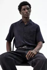 Camisa negra de manga corta con cuello resort, tapeta lisa, bolsillo superior y canesú en la espalda.