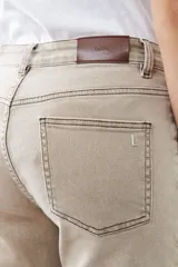 Pantalón de jean color beige, de corte recto, con bolsillos laterales y traseros. Se ajusta a la cintura con cinturón de cuero marrón.