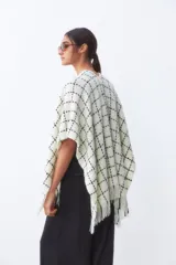 Ruana color crudo con diseño de cuadros negros y flecos en el borde inferior.