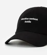 Gorra de sarga negra con visera curva y bordado frontal en blanco que dice "sensitive content inside".
