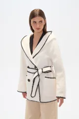 Chaqueta color crema con ribete negro en contraste, corte holgado, cuello en V, cierre cruzado con botones y lazo para atar.