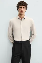 Camisa color beige de corte slim fit, confeccionada en tejido elástico con cuello italiano abierto, manga larga con puños abotonados y cierre frontal con botones.