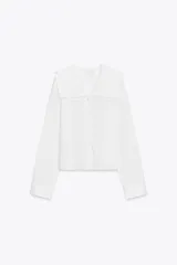 Camisa blanca de algodón con cuello bobo, manga larga con puños y cierre frontal con botones.