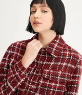 Campera corta de tweed a cuadros en tonos rojo, blanco y negro. Tiene cuello clásico, cierre frontal con botones, dos bolsillos en el pecho y flecos en el dobladillo.