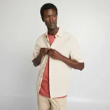 Camisa de manga corta color beige claro, con cuello clásico y cierre frontal con botones. Confeccionada en mezcla de lino.