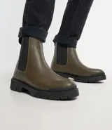 Bota Chelsea color verde oliva, confeccionada en cuero sintético, con laterales elásticos negros y suela track negra.