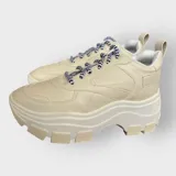 Zapatillas deportivas color beige con cordones a rayas en blanco y negro, suela de goma con plataforma y diseño chunky.