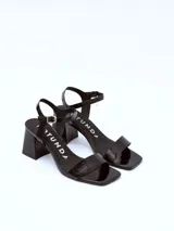 Sandalias de cuero charol negro con tira delgada sobre los dedos, pulsera con hebilla al tobillo y tacón cuadrado.