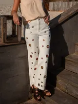 Pantalón de jean blanco de tiro alto con corte recto y ojalillos metálicos grandes a lo largo de las piernas.