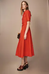 Vestido midi camisero color ladrillo, confeccionado en popelina de algodón. Presenta cuello solapa, manga corta con puños abotonados, bolsillos laterales ocultos y bolsillos de parche con solapa en el pecho. Incluye cinturón lazada en el mismo tejido y cierre frontal con botones ocultos.