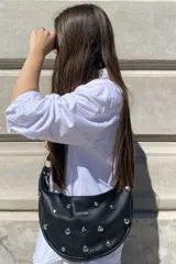 Cartera bandolera negra con forma de media luna, con tachas plateadas y logo de la marca en el frente.
