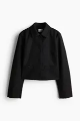 Campera corta negra con cuello clásico, hombros ligeramente caídos, bolsillos decorativos delanteros y forro interior.