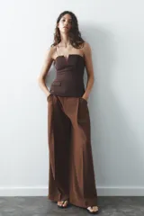 Pantalón color ladrillo de tiro medio con trabillas, detalle de pliegues, bolsillos laterales y falsos bolsillos de vivo en la espalda. Cierre frontal con cremallera y botón.