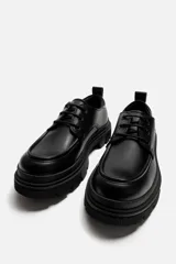 Zapato de vestir tipo blucher color negro, con detalle de bordón, tirador trasero y suela con volumen irregular.