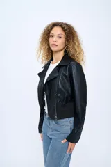 Campera corta de cuero sintético negro, estilo motoquero, con cuello clásico, cierre asimétrico con cremallera, bolsillos laterales con cremallera y puños con cremallera.
