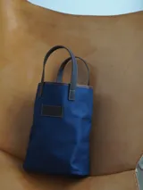 Bolso matero de lona color azul con detalles en cuero marrón, con asas cortas y logo de la marca en cuero.